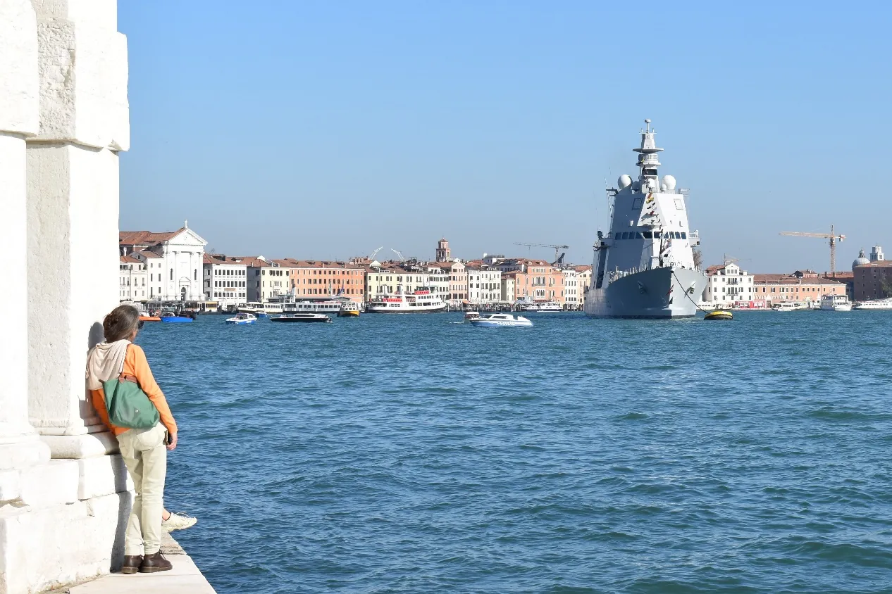 Una persona che osserva il mare e una nave militare a Venezia, immagine evocativa per il contesto letterario e poetico di Gianfranco Pancino.