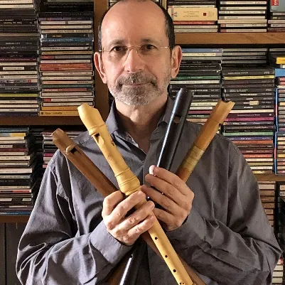 Il musicista Goffredo Degli Esposti ritratto davanti a una collezione di CD mentre regge diversi tipi di flauti antichi.