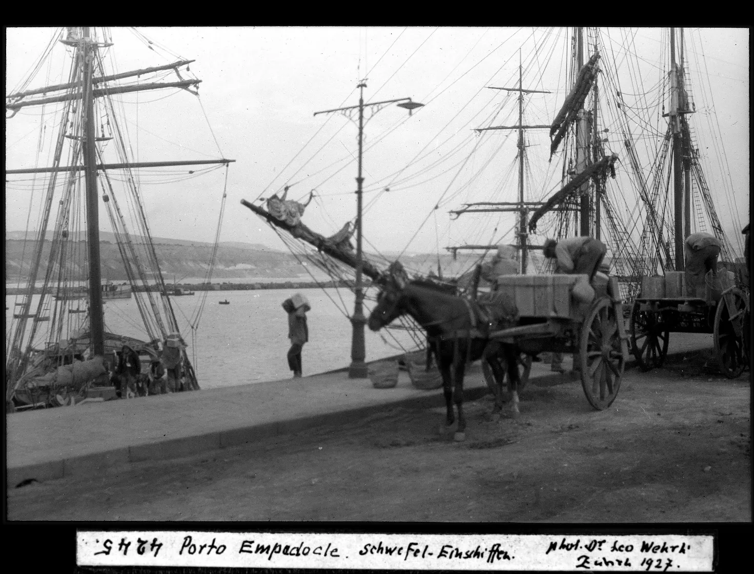 Fotografia d'epoca del 1927 che ritrae il porto di Porto Empedocle con navi e carretti carichi di zolfo, un importante documento storico legato ai luoghi di Andrea Camilleri.
