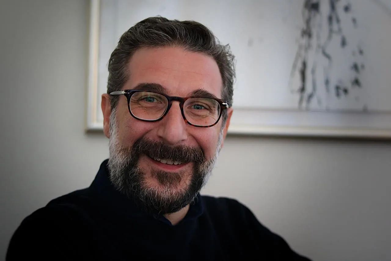 Primo piano del compositore Mauro Montalbetti che sorride, protagonista dell'intervista sulla musica e la felicità su Finnegans.